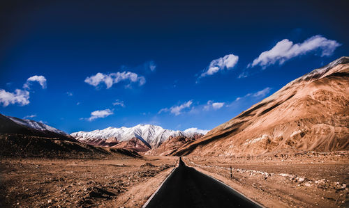 Road amidst snowcapped mountains against blue sky