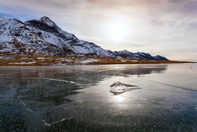 Scenic view of frozen lake by snowcapped mountains against sky