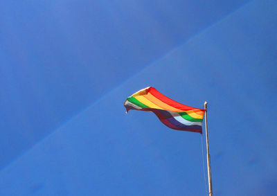 Low angle view of rainbow flag waving against blue sky