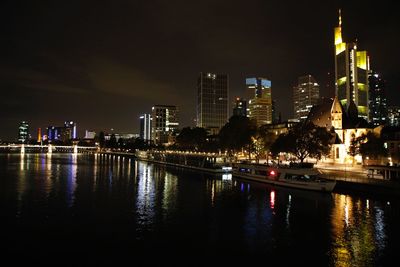 Illuminated buildings by river against sky at night