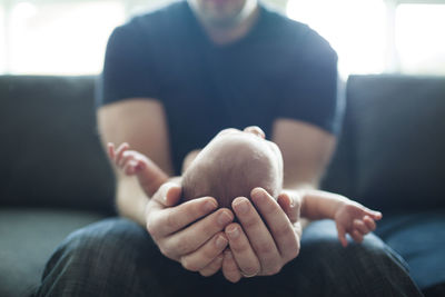 Midsection of father holding newborn baby while sitting at home