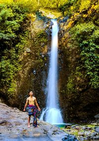 Full length of man standing by waterfall in forest