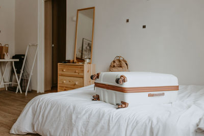 White suitcase and beige backpack on the white bed at home