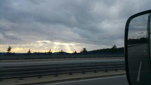 Cars on road against cloudy sky