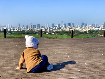 Rear view of woman sitting on beach against clear sky