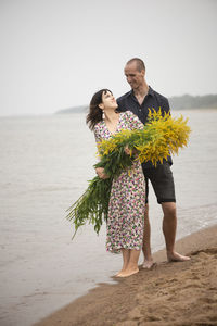 Young romantic couple with big bouquets of wild flowers posing on the beach