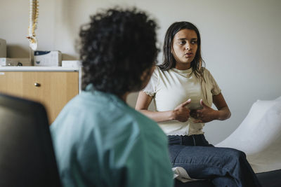 Young woman touching abdomen and inhaling during medical exam in clinic