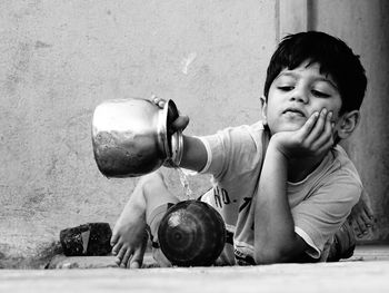 Boy pouring water from lota on ball while lying by wall