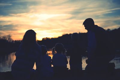Family sitting on field against lake during sunset