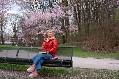 Mature woman sitting on a bench in the park and working on the tablet.