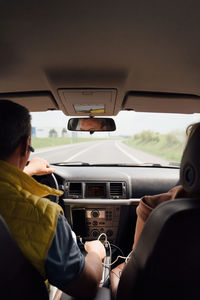 Side view of concentrated adult male in puffer jacket and hands free headset driving modern car on asphalt road on cloudy day in countryside