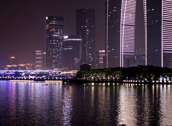 Illuminated buildings by river against sky at night