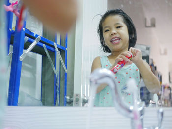 Smiling girl holding toothpaste while standing against mirror 