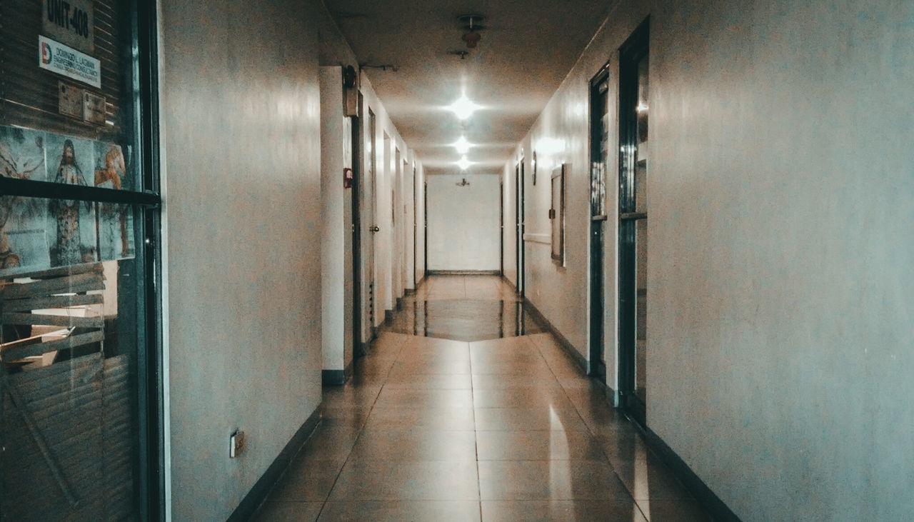 EMPTY CORRIDOR ALONG ILLUMINATED BUILDING