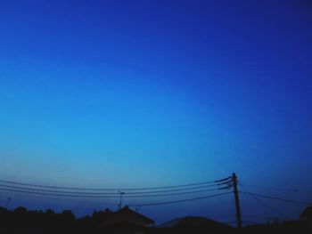 Low angle view of silhouette electricity pylon against clear blue sky