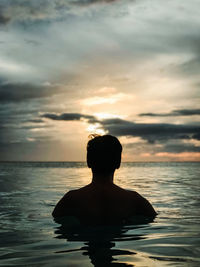 Rear view of silhouette man swimming in sea against sky at sunset