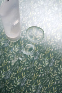 A transparent bottle of cosmetic gel on a green background with drops of the product.