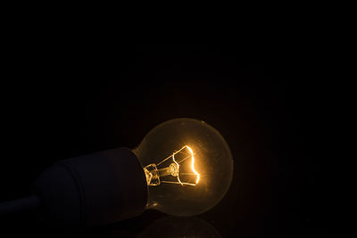 Close-up of hand holding illuminated light bulb in darkroom