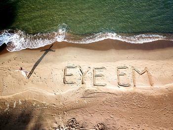 Drone shot of woman standing by eyeem text on sea shore