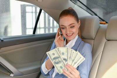 Smiling businesswoman holding paper currency while sitting in car