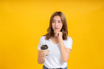 Portrait of beautiful young woman standing against yellow background