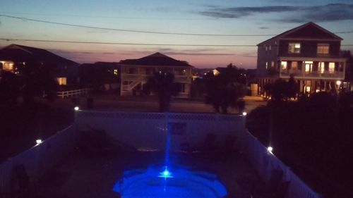 Illuminated city by building against sky at dusk