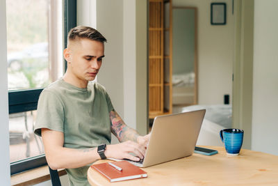 Happy young man working at home with laptop sits in the living room at home in the morning.