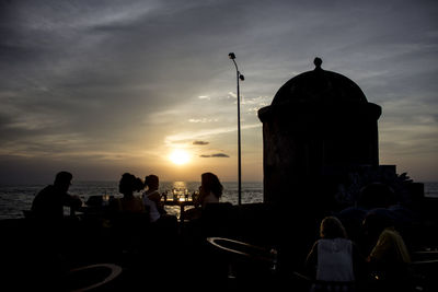 People sitting at outdoors cafe by sea during sunset