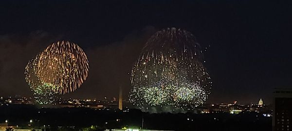 Firework display over city against sky at night