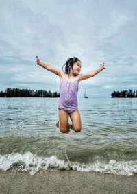 Full length of a young girl doing yoga at beach against sky