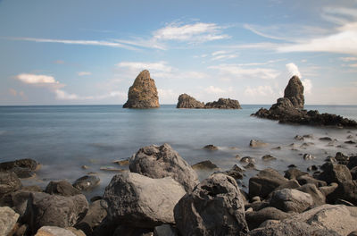 Rocks on shore by sea against sky