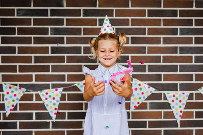 Portrait of smiling girl standing against brick wall