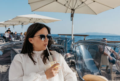 Front view of a young woman sitting and drinking juice on terrace in cafe by sea in opatija.