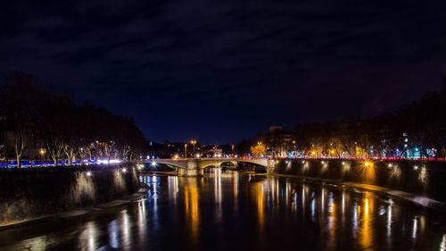 Illuminated bridge over river against sky at night