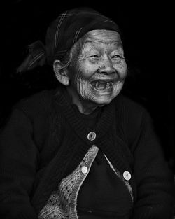 Close-up of senior woman laughing against black background