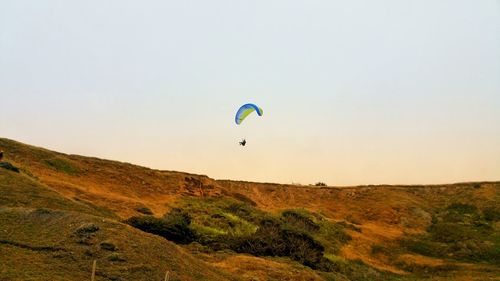 Person paragliding against golden cliffs and clear sky