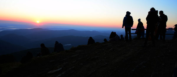 Silhouette people standing on mountain against sky during sunset