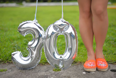 Low section of woman holding balloons while standing on field