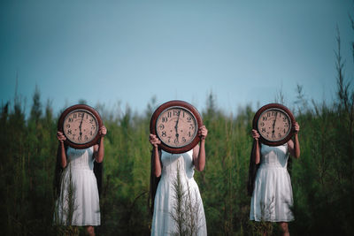 Women with wall clocks standing against plants