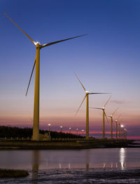 Wind turbines by lake against sky during sunset