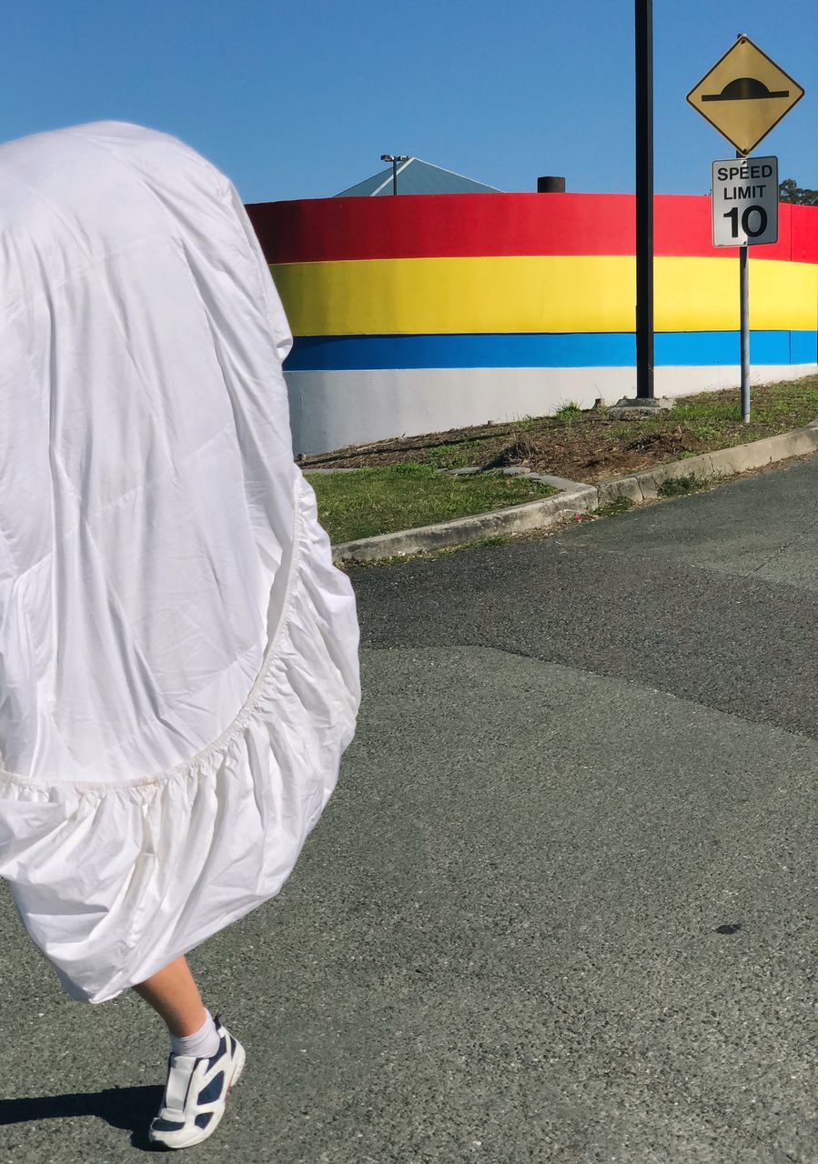 road, transportation, day, sign, one person, real people, symbol, communication, city, street, road sign, walking, nature, multi colored, outdoors, sky, full length, motion, lifestyles