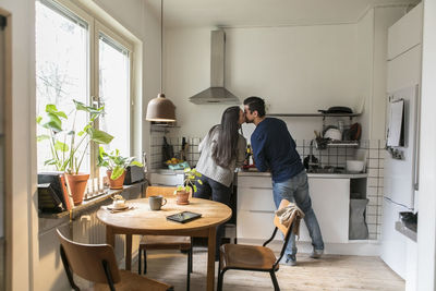 Smiling couple kissing while working in kitchen at home