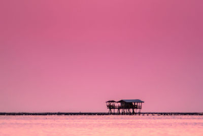 Silhouette built structure on sea against clear sky