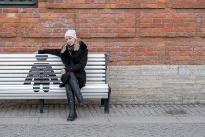 Side view of young woman sitting against brick wall