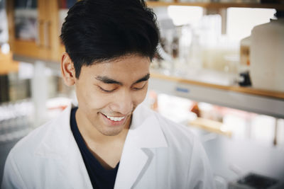 Smiling young male university student looking down at chemistry laboratory