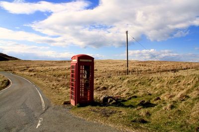 Telephone booth by field against sky