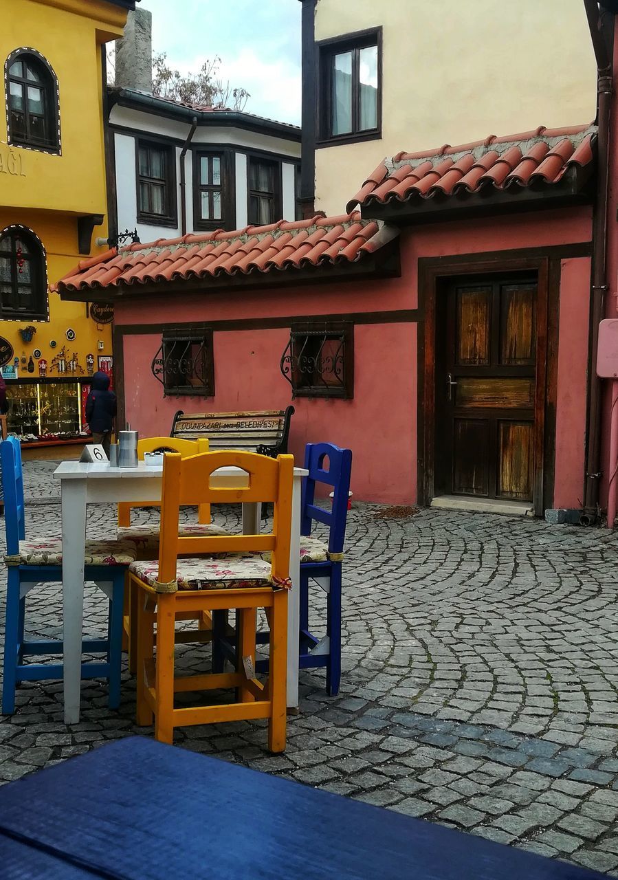 EMPTY CHAIRS AND TABLES IN STREET BY BUILDINGS