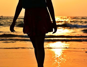 Midsection of silhouette woman walking at beach during sunset