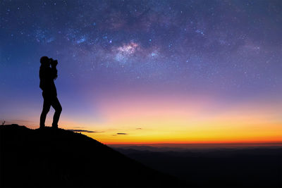 Silhouette person photographing sky at night