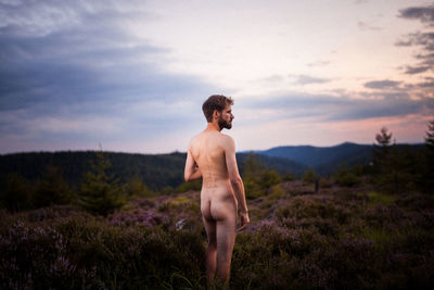 Rear view of naked man standing on field against sky